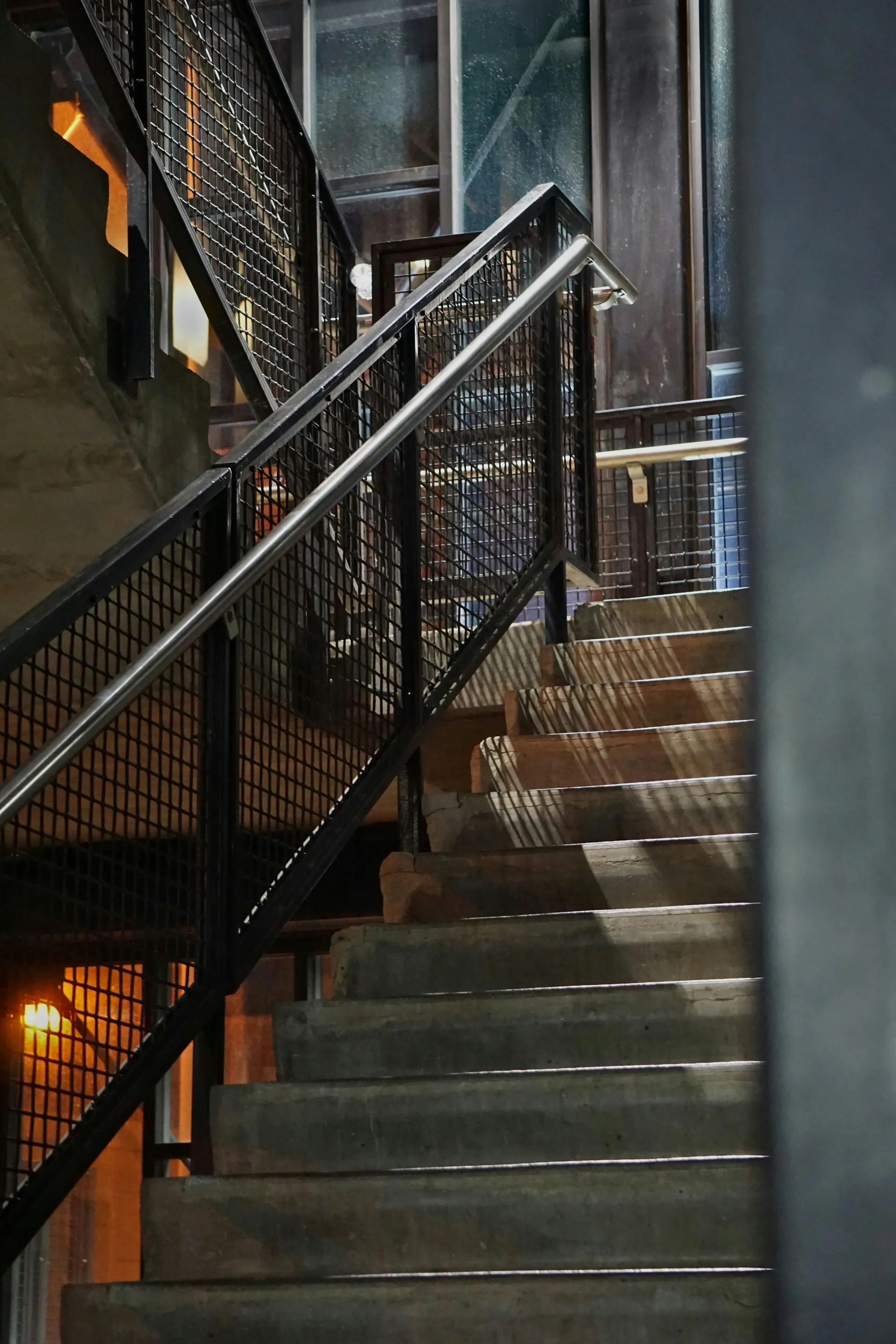 Průmyslové betonové schodiště v exteriéru vybavené robustním černým kovovým zábradlím s výplní z drátěného pletiva.